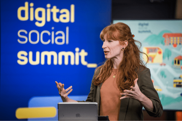 Eine Frau steht vor einem Aufsteller mit der Aufschrift Digital Social Summit an einem Pult, sie gestikuliert.