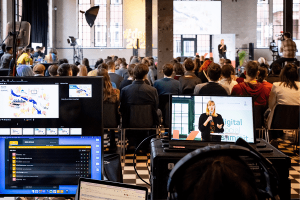 Auf dem Foto vom Digital Social Summit ist der Blick ins Publikum und auf die Bühne vom Livestream-Desk aus zu sehen.