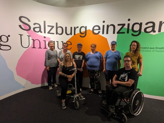 Mehrere Menschen mit und ohne sichtbare Behinderung haben sich zum Gruppenbild aufgestellt. Dahinter ein Banner, auf dem steht: Salzburg einzigartig.