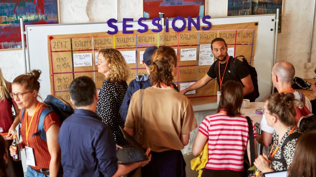 Eine Menschentraube steht vor einer Wand, auf der Sessions steht.