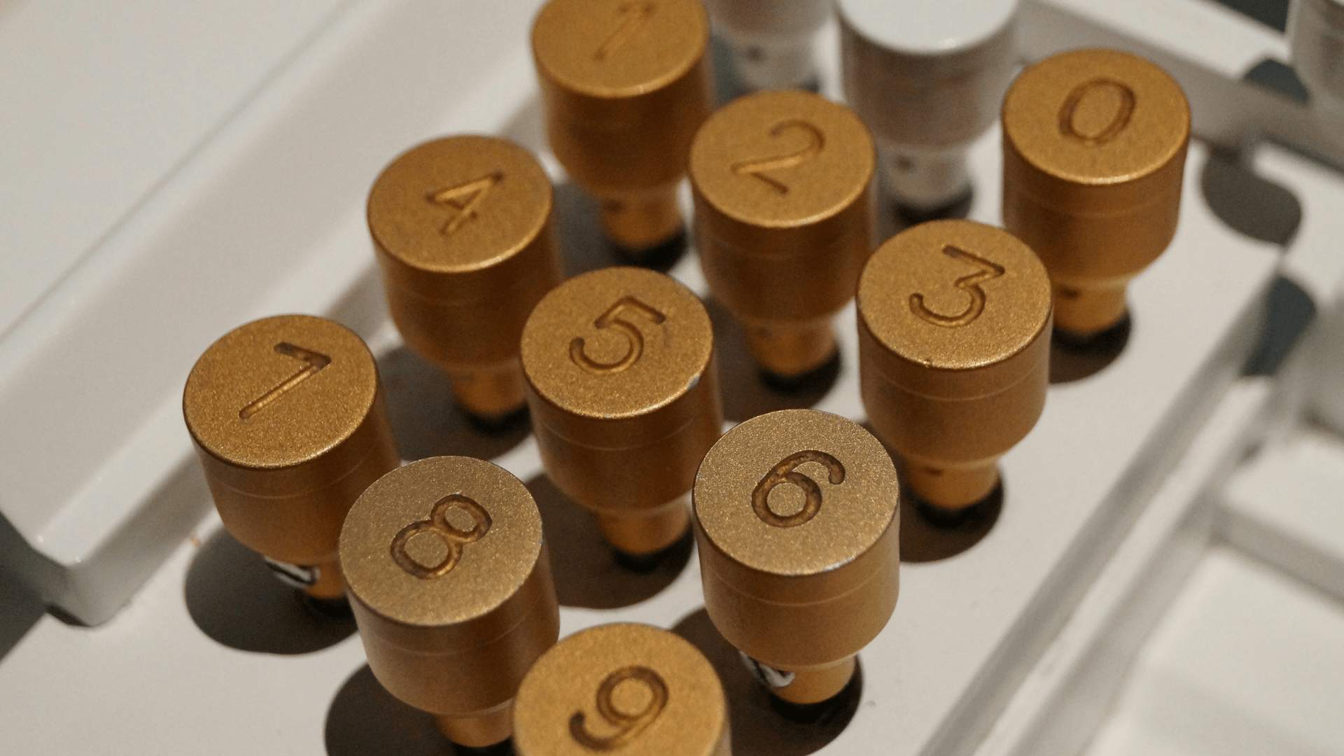 Angeordnet wie auf einem Taschenrechner, sieht man runde Tasten mit den Zahlen 0 bis 9 aus Messing.